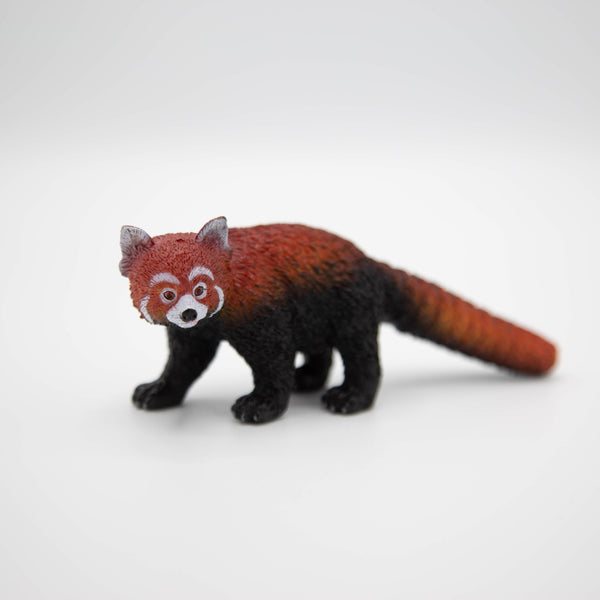 A small plastic red and brown red panda toy model on all fours, with a long tail and white face