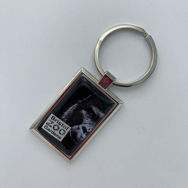 A metal keyring showing half the face of a gorilla with the Bristol Zoo Gardens logo in the left corner.