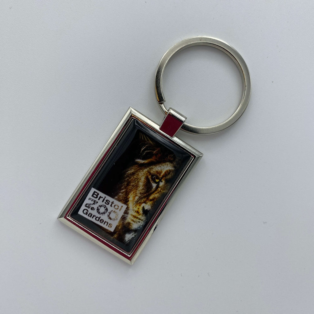 A metal keyring showing half the face of a lion with the Bristol Zoo Gardens logo in the left corner.